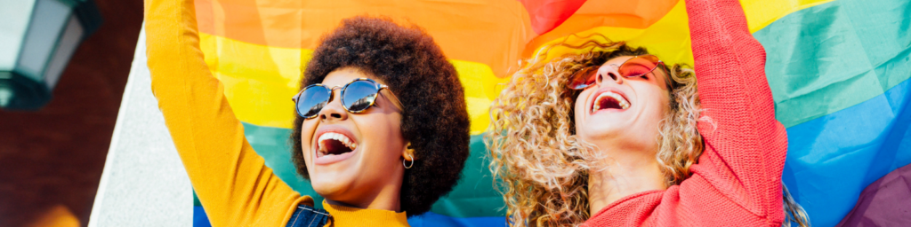A black woman and a white woman smiling and holding a pride flag